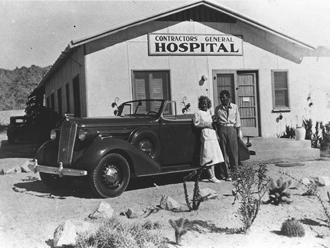 Betty Runyen and Sidney Garfield leaning on car in front of Contractors General hospital black and white