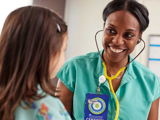 A nurse wearing a stethoscope smiling at her child patient.